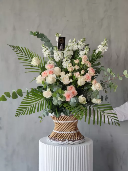 This stunning bouquet of flowers in a small wicker stool is the perfect way to brighten up any room. Soothing to the eyes, the arrangement features a variety of blooms in pastel shades. The flowers are arranged in a rustic wicker base, which adds to the overall charm of the bouquet. This arrangement  is perfect for any occasion, whether you're looking for a gift for a loved one, a centerpiece for a special event, or simply want to add a touch of beauty to your home décor. 