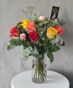 A lovely glass vase filled with a beautiful arrangement of vibrant roses in a variety of colors. This centerpiece is perfect for any occasion, from a birthday to an anniversary to a simple day of appreciation.